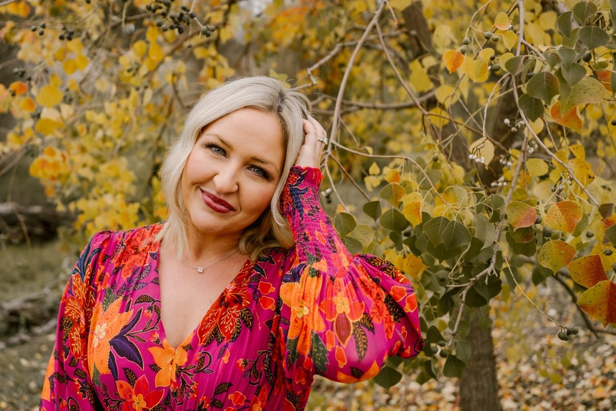 Adele in a bright floral dress in front of fall leaves